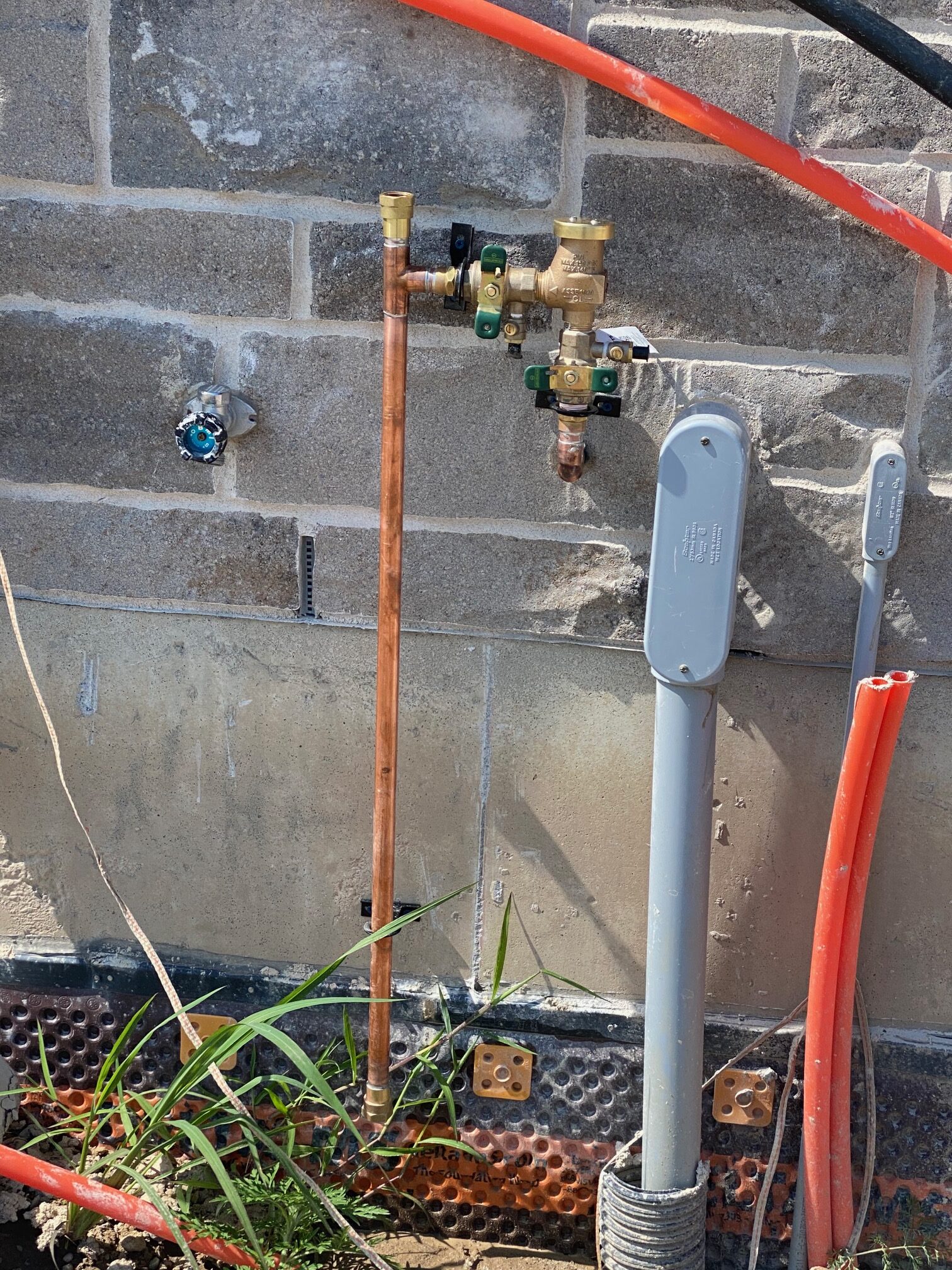 Pressure vacuum breaker backflow prevention assembly connected to soldered copper piping on a home's exterior or utility wall.