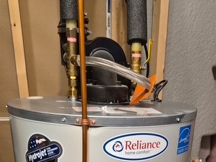 Cash Acme thermostatic mixing valve assembly installed on top of a water heater tank with brass fittings and stainless steel braided supply line in London, Ontario.