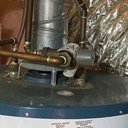 Aging Watts thermostatic mixing valve installed on top of an old natural draft gas water heater before replacement in London, Ontario.