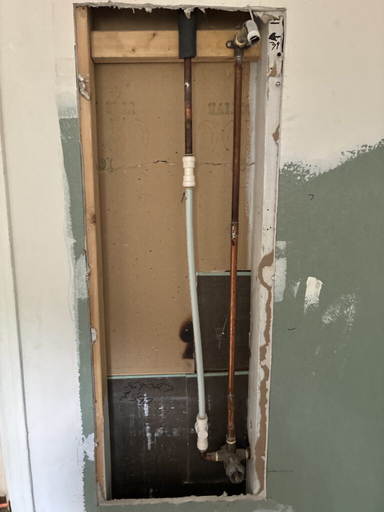 Exposed bathroom wall framing showing an old shower valve connected with temporary push-fit plumbing fittings in a St. Thomas, Ontario home.