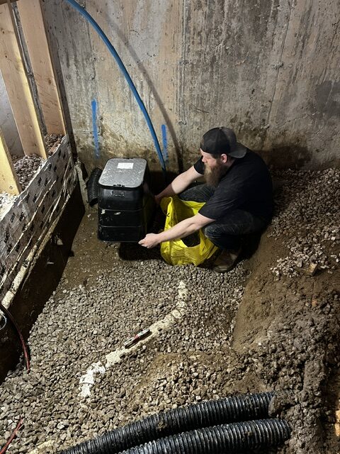 Plumber Aaron K setting up a sewer backwater valve with protective access sleeve in a basement excavation for a new home in Oak Park, London, Ontario.
